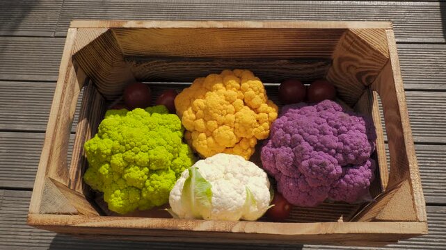 Top view of Colorful cauliflower heads in wooden crate with cherry tomatoes, carefully arranged for vibrant culinary presentation highlighting natural textures, vivid seasonal produce, wholes
