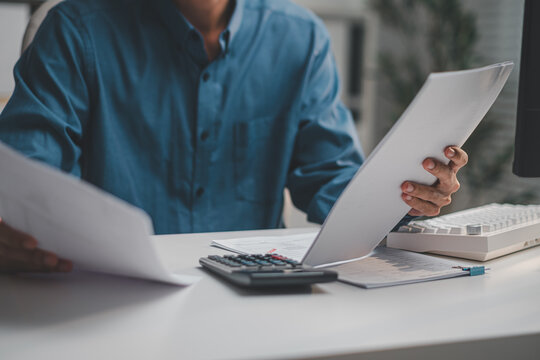 Accountant comparing financial reports and tax documents with calculator on office desk.