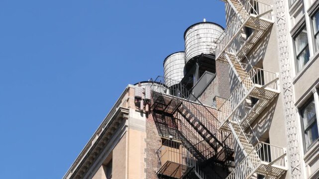New York City urban building architecture, Manhattan rooftop, United States of America. Water tower on roof. Classic water tanks. Fire metallic ladder or fire escape. Blue sky.