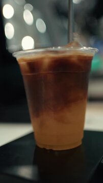 Barista stirring a cold coffee drink with orange juice and ice in a plastic cup, creating a refreshing citrus coffee beverage