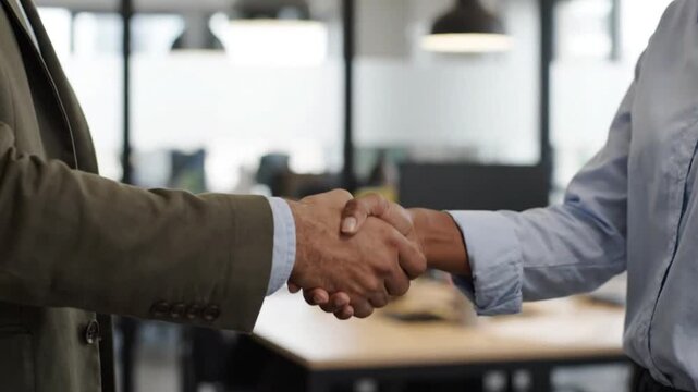 Successful negotiation displays professional commitment as two business partners seal a contract with a firm handshake in a sleek corporate office.