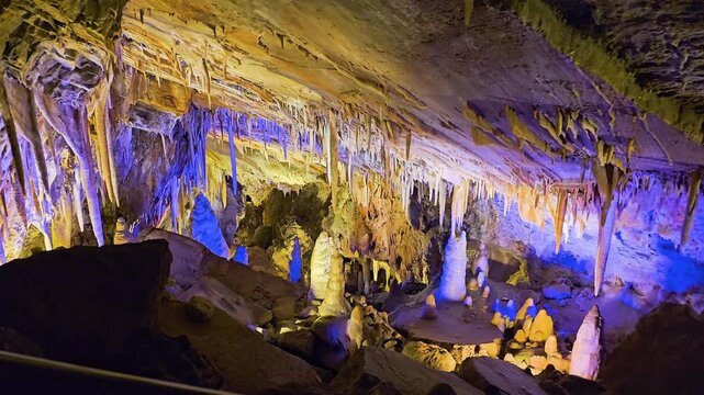 Ancient cavern ceiling covered in delicate stalactites and mineral deposits, illuminated by spotlights that reveal layered limestone textures, shadows, and natural underground formations.