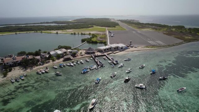Aerial view pulling back from Los Roques airport, showing boats, pier, and coastline