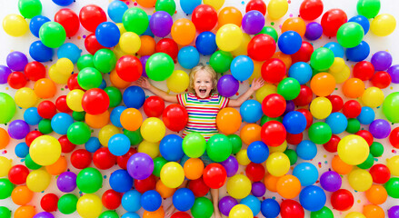 Obraz premium Happy young child lying in a pool of colorful balloons, joyful expression, bright festive atmosphere. Celebration, birthday, childhood joy, party concept.