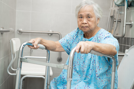Caregiver help Asian elderly woman patient use walker and toilet bathroom handle security.