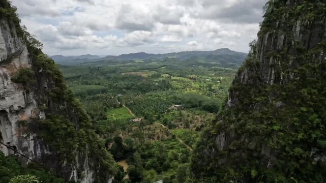 Expansive view of a verdant valley framed by majestic limestone mountains in Chumphon, Thailand.