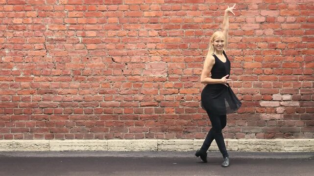 Blonde dancer poses expressively against red brick wall outdoors