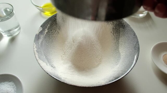 Baker sifting white wheat flour with sieve into bowl on kitchen table