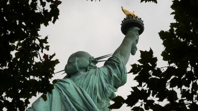 Statue of Liberty on Liberty Island, New York, United States. Cooper monument, symbol of democracy and patriotism near Manhattan, NYC USA. American independence. Autumn fall leaves. From behind, back.