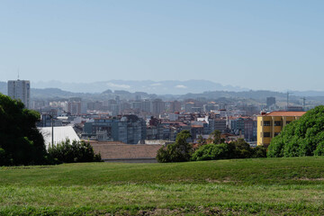 Green grassy hill overlooks the rooftops and apartment blocks of Gijon in Spain with hazy mountains on the horizon. Urban skyline panorama for travel, real estate and city development themes. © Renata