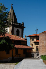 Stone bell tower topped with a cross rises above terracotta roofs and a brick wall in the old town of Gijon, Spain. Rooster weather vane and sunlit facades suit travel and heritage tourism themes. © Renata