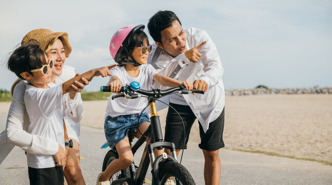 As sun sets happy father mother and daughter embrace joy of summer road trip on sandy beach. Teaching and learning bicycle riding become cheerful and heartwarming family experience.