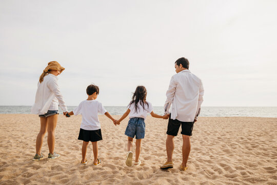 Happy parents holding hands running with their children on the beach and jumping in joy. A heartwarming scene of family togetherness and carefree fun capturing the essence of a beach vacation.