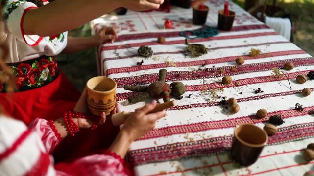 Ukrainian women perform witch rituals while dressed in vyshyvankas. They gather herbs and create patterns on a table in a natural setting. The focus is on their cultural practices.