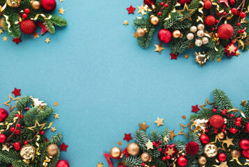 Obraz premium Christmas and New Year celebration arrangement on blue background with green fir branches, shiny decorations, confetti stars ornaments top view.