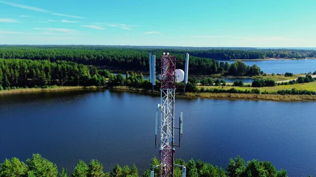 Telecommunication tower with antenna overlooking serene lake and lush green forest landscape