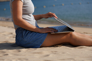Woman opens a laptop while sitting on a sandy beach, creating a remote work scene for freelance, digital nomad, travel, online business and flexible workplace themes. © soya