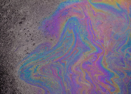 Iridescent oil slick on wet asphalt, colorful gasoline spill texture, rainbow fuel puddle