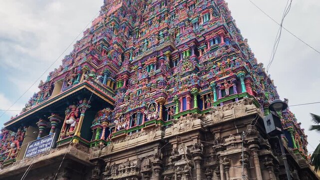 4K video panning upward from the base to the top of the ornate gopuram of Meenakshi Amman Temple in Madurai, Tamil Nadu, India, revealing intricate sculptures and colorful Dravidian architecture.