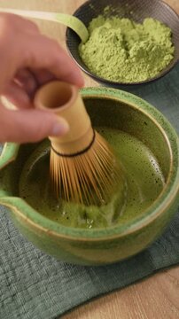 Whisking green matcha tea with traditional bamboo whisk chasen in ceramic bowl chawan to create foam. Preparing authentic Japanese matcha tea, healthy wellness beverage and detox drink.