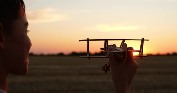 Child holds toy airplane at sunset in field. Young dreamer imagines flight as golden light shines through vintage biplane. Nostalgic childhood adventure inspires aviation dreams and freedom.