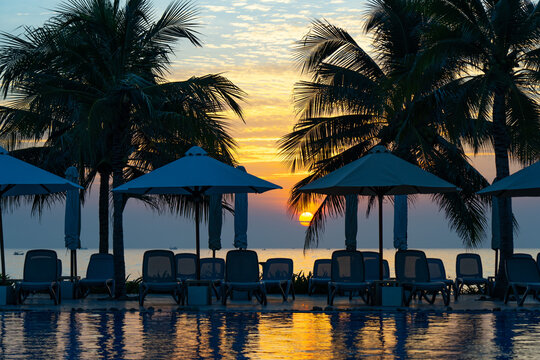 Serene Sunset Over a Tropical Poolside Retreat with Palm Trees, Umbrellas, and Reflections in Calm Waters
