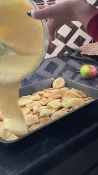 Vertical close up of cake batter poured over apple slices for charlotte, homemade autumn dessert preparation