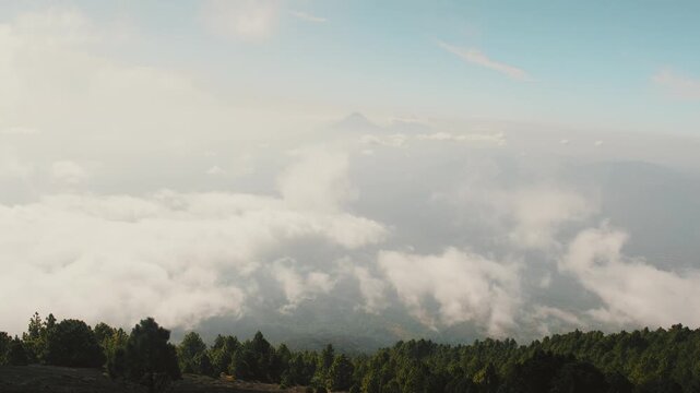 Dramatic clouds rolling above lush pine forest on Acatenango volcano, Guatemala. Crisp morning light, panoramic wide shot, breathtaking sky perspective.