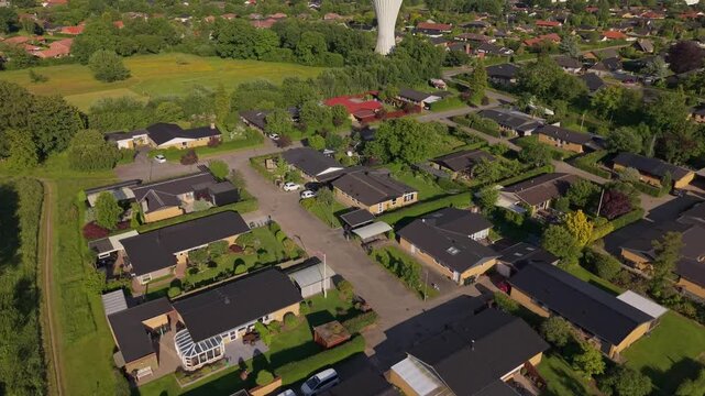 Aerial footage rising above Kolding's suburban neighborhoods to reveal the distinctive water tower, with lush greenery and the picturesque Danish cityscape in the background.