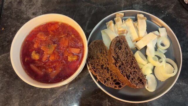 Homemade red borscht served beside salo, onion and rye bread, hearty traditional Eastern European meal on a table