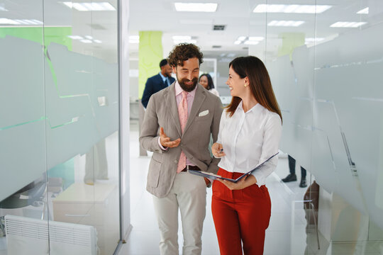 Diverse business professionals walking through a modern office corridor. Smiling and engaging in conversation. Representing successful teamwork. Collaboration
