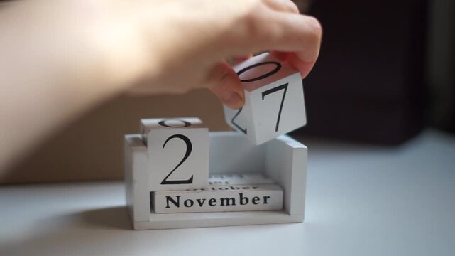 Black Friday Close up shot of white wooden calendar blocks displaying 27 November, held by hand, cardboard box in background buy sales cheap prices consumption shopping mail boxes