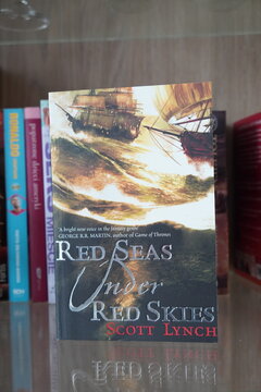 A copy of the fantasy novel Red Seas Under Red Skies by Scott Lynch displayed on a glass shelf
