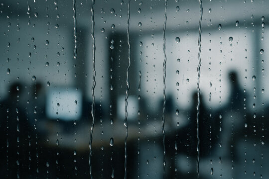 Raindrops run down glass before a blurred office interior