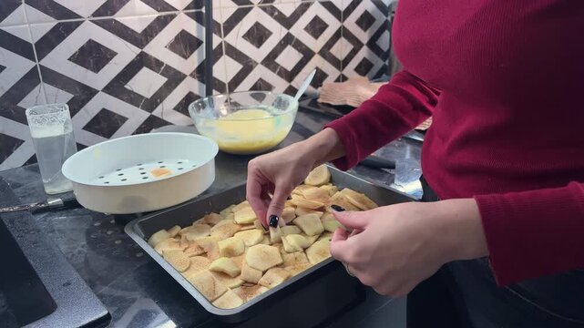 Woman places fresh apple slices evenly on a baking tray, step in preparing a homemade fruit cake