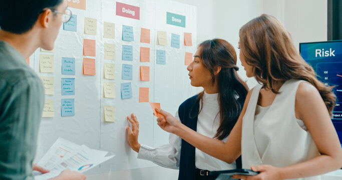 Group of Asian businesspeople work together collaborating and sharing ideas use colorful note on wall in business meeting in office. Financial generation z team brainstorm on e-Commerce project.