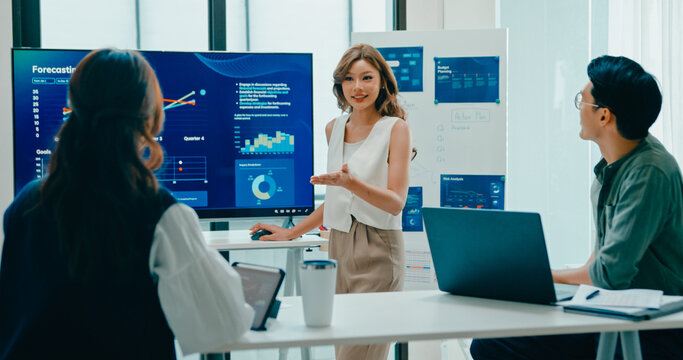 Group of Asian businesspeople work together leads business meeting uses presentation TV with revenue, profit or sale statistics in office. Financial generation z team brainstorm on e-Commerce project.