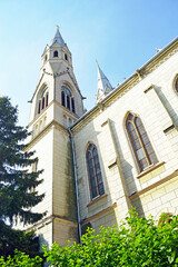 Exterior of Sacred Heart Church Timisoara with pointed spire, arched stained-glass windows, and decorative cornices. Conveys verticality of sacred architecture and Romanian urban tourism attraction. © tanyatorgonskaya