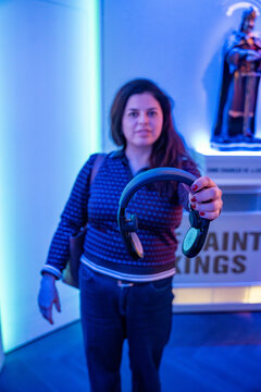 Woman holding audio guide headphones inside museum exhibition space. Interactive cultural tourism experience and self guided museum tour concept.
