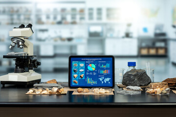 Microscope, rock samples and fossils beside a tablet showing colorful scientific charts in a modern geology laboratory. © NanSan
