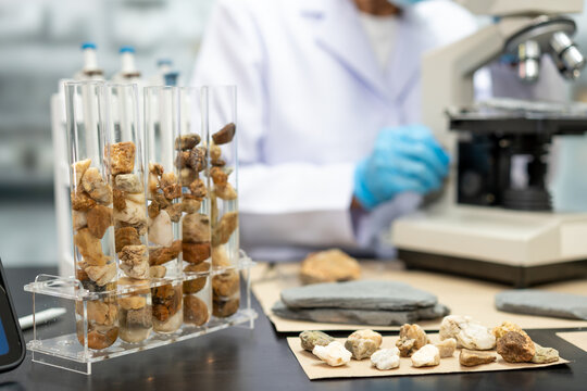 Geologist examines rock and mineral samples in test tubes beside a microscope in a modern laboratory, supporting research, testing, and scientific analysis.