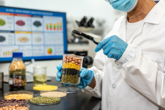 Food scientist in a laboratory examines a clear jar of layered legumes with a magnifying glass during quality testing and nutrition research.