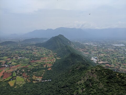 Scenic rural landscape with green farmlands and mountain slopes under a hazy sky.