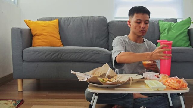 Young man pours water into glass of orange juice while enjoying traditional Indonesian salad dish