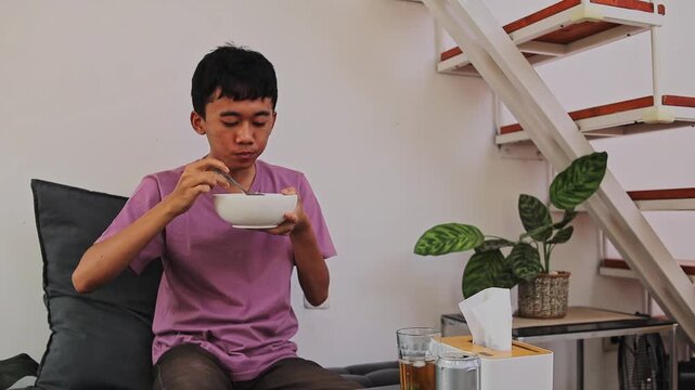 Young Asian man holding bowl and eating batagor kuah with spoon
