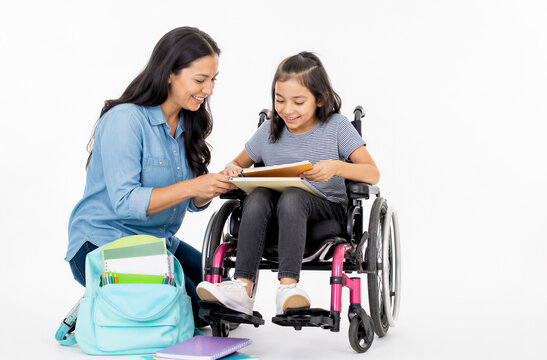 Woman helping young girl in wheelchair with schoolwork, sitting together with backpack and notebooks, bright studio lighting. Education, disability inclusion, learning, childhood.