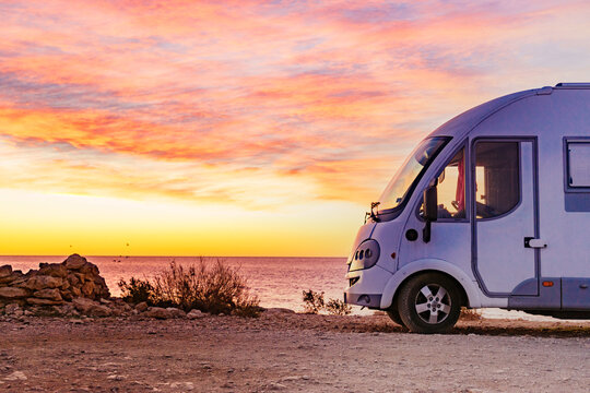 Warm sunset view at the beach with a camper van parked along the shore by the water