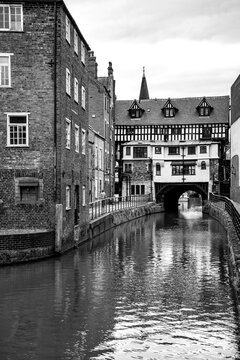 The medieval Glory Hole spanning the River Witham in Lincoln, England, surrounded by historic buildings. Atmospheric black and white cityscape.