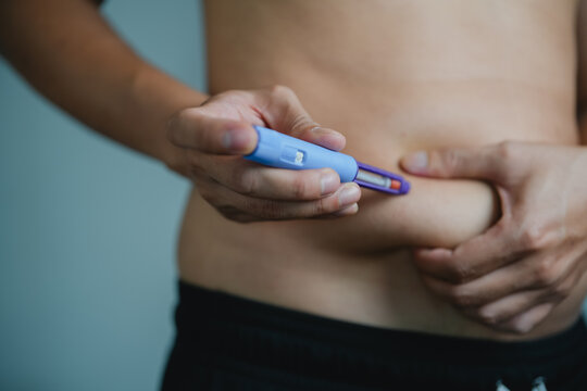 Man giving herself auto-injector injection in abdomen for biologic allergy therapy, GLP-1 weight loss medication, or chronic medical treatment 
