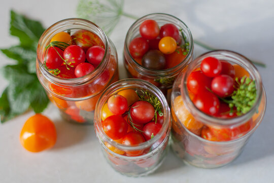 Top view of assorted fresh cherry tomatoes in glass jars, prepared for home canning and pickling. Summer harvest and traditional home preservation. Organic food, gardening, seasonal preparation.